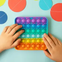 Dziecko bawi się kolorową zabawką sensoryczną typu pop it na jasnoniebieskim tle z girlandą kółek.