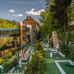 Mini golf z miniaturami znanych budowli, w tym Krzywej Wieży w Pizie, na tle hotelu i lasu.