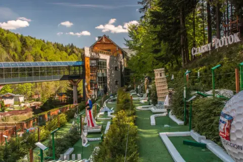 Mini golf z miniaturami znanych budowli, w tym Krzywej Wieży w Pizie, na tle hotelu i lasu.