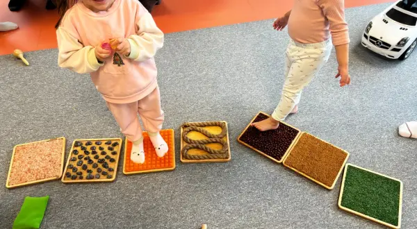 Dzieci stąpają po sensorycznych matach z różnymi fakturami, wspierając integrację sensoryczną.