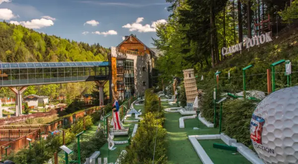 Mini golf z miniaturami znanych budowli, w tym Krzywej Wieży w Pizie, na tle hotelu i lasu.